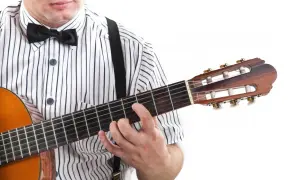 Mężczyzna w muszce i koszuli w paski gra na gitarze, trzymając palce na gryfie. Widoczne są tabulatury na gitarę.