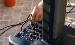 Ręka podłącza kabel do miksera, pokazując, jak podłączyć przedwzmacniacz do wzmacniacza.
