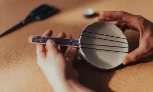 Dziecko tworzy proste instrumenty muzyczne: ukulele z talerzyka i gumek.