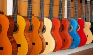 Rząd kolorowych instrumentów akustycznych, w tym gitar w odcieniach pomarańczu, żółci, czerwieni i niebieskiego, wisi na drewnianej ścianie.